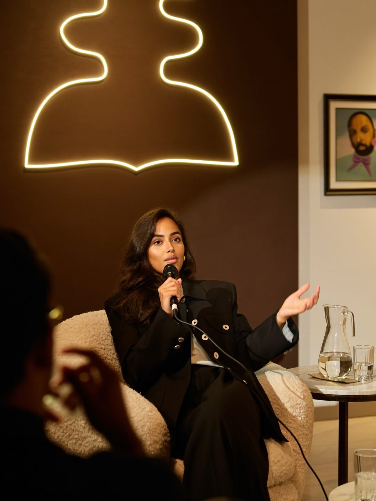 Speaker in an armchair at an intimate brand fireside event, warm editorial light