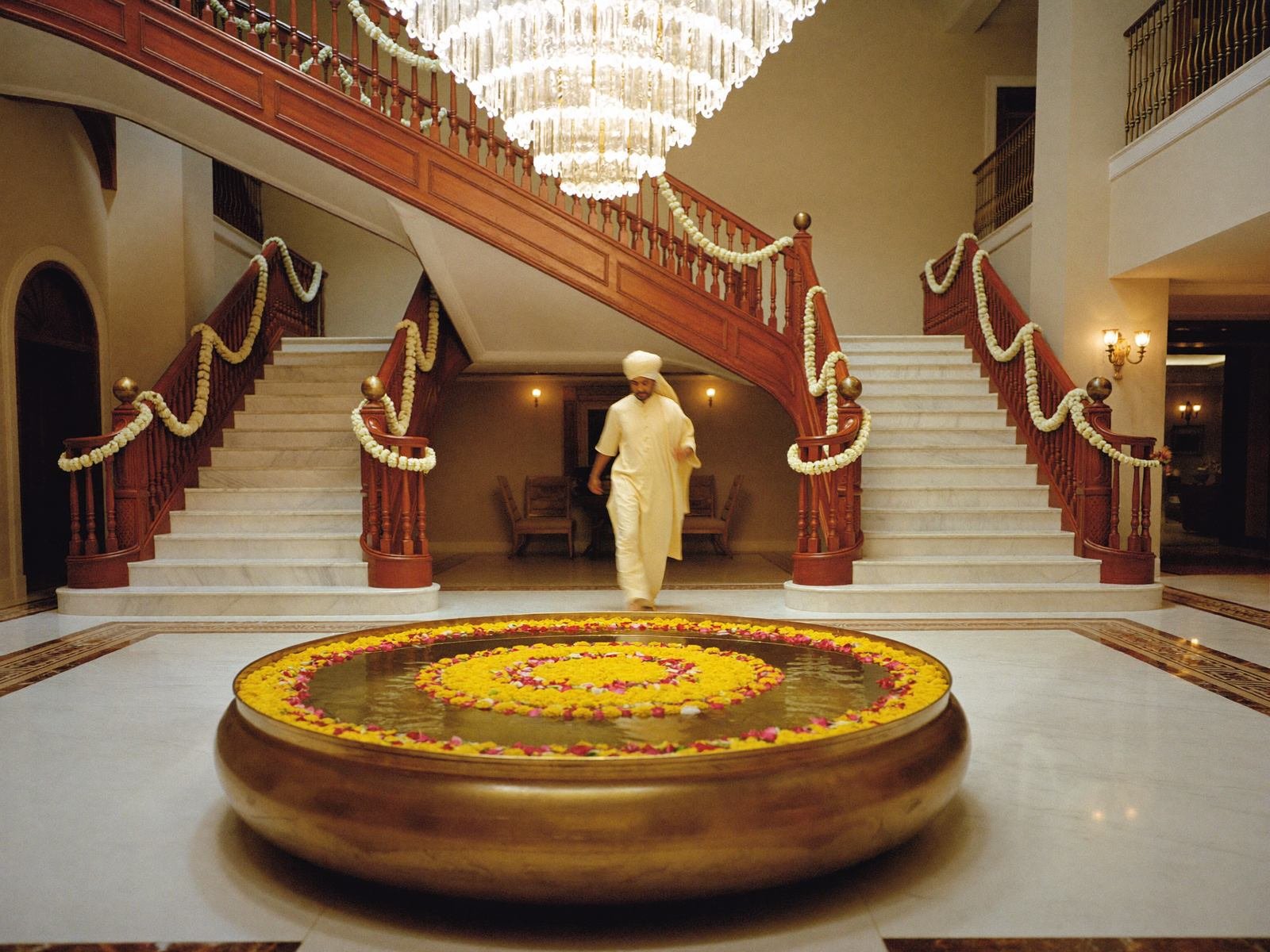 Indian five-star hotel lobby with brass urli of flowers, garlanded staircase and chandelier