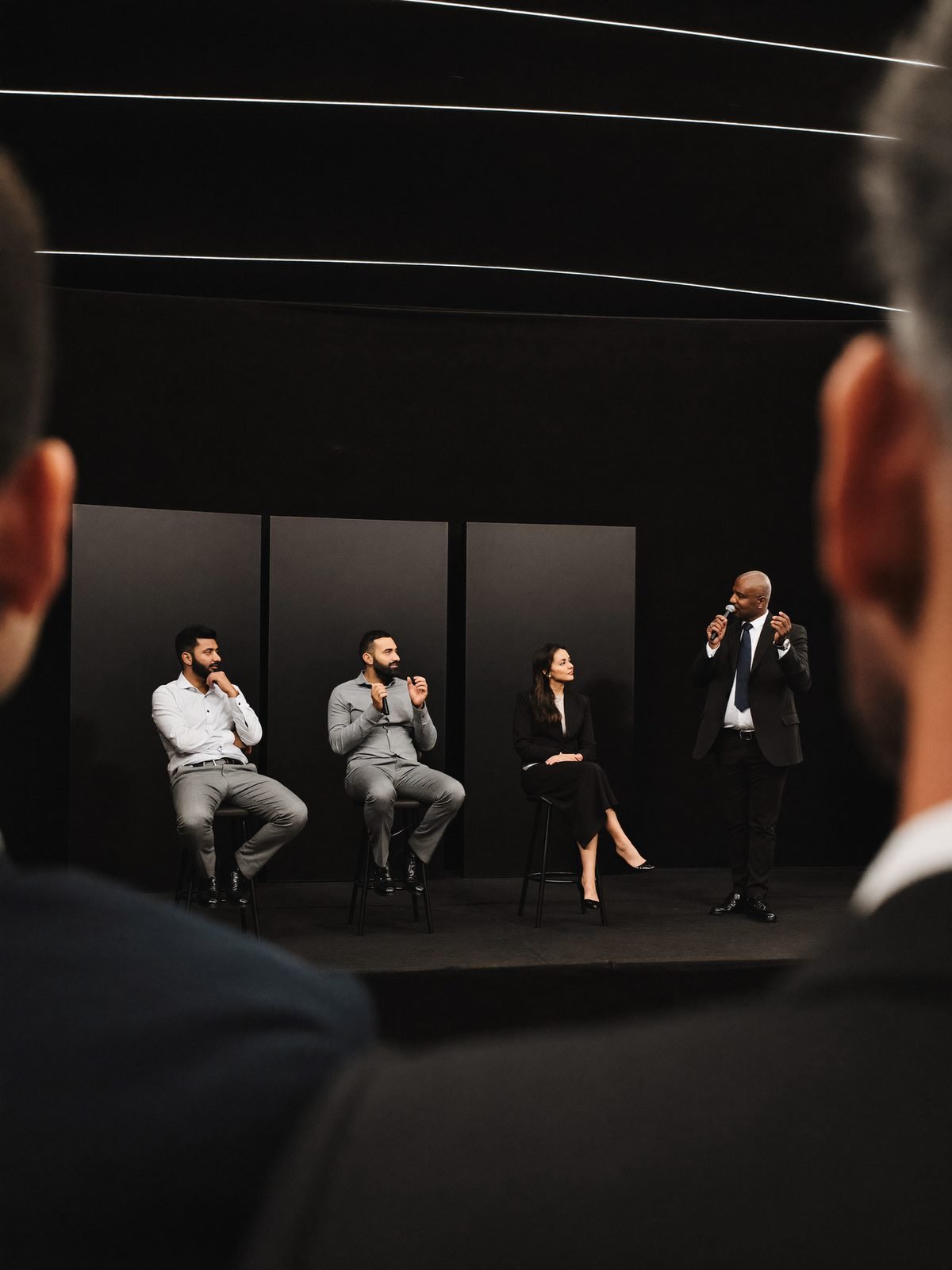 Panel discussion on a dark premium stage, photographed from within the audience
